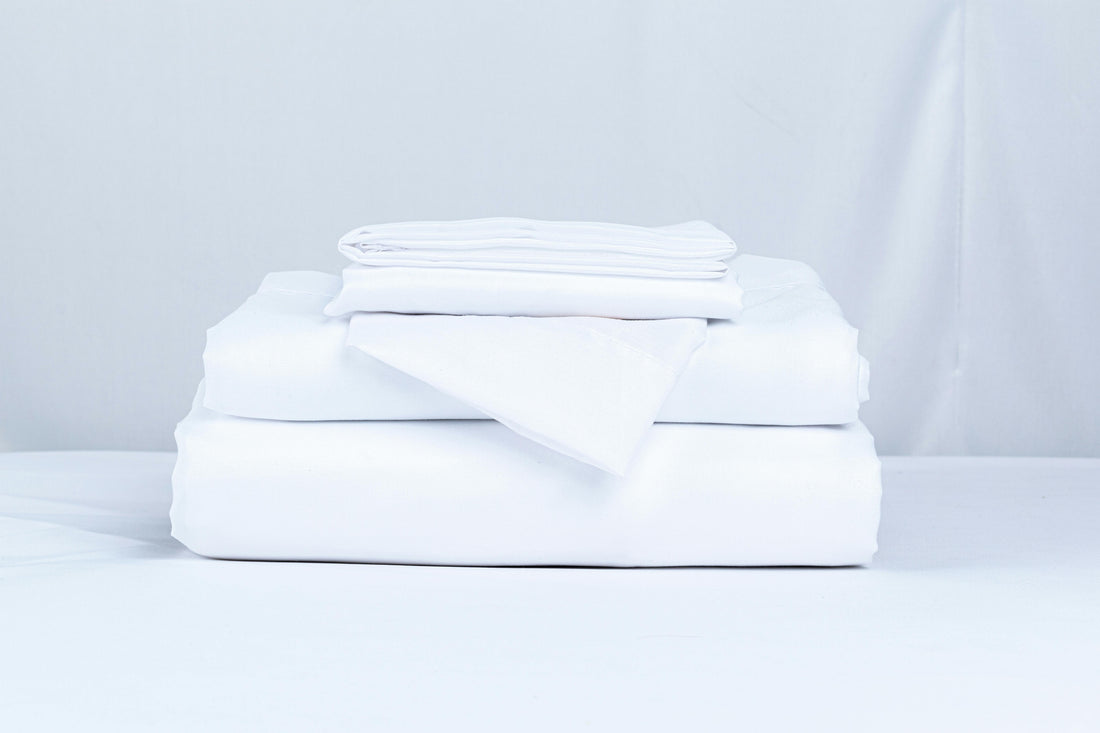 A neatly folded stack of crisp white bed linens in soft natural light — illustrating Fragrenza's edit of the best clean laundry perfumes.