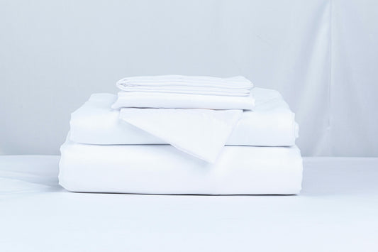 A neatly folded stack of crisp white bed linens in soft natural light — illustrating Fragrenza's edit of the best clean laundry perfumes.