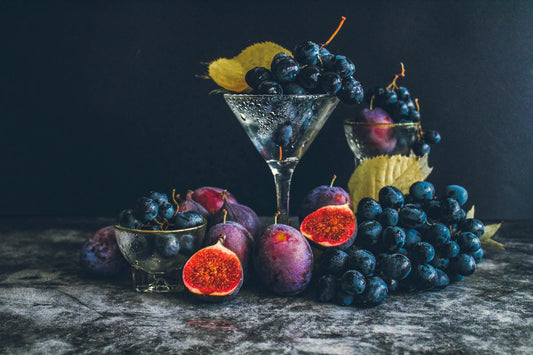 Variety of dark autumn fruits in moody warm light — the plum-and-fig direction defining fall 2026 perfumery